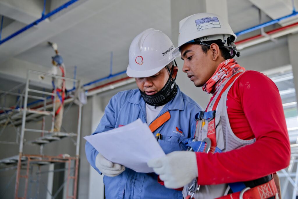 pexels photo 1216589 1216589 Two engineers in safety helmets reviewing construction plans at a worksite.